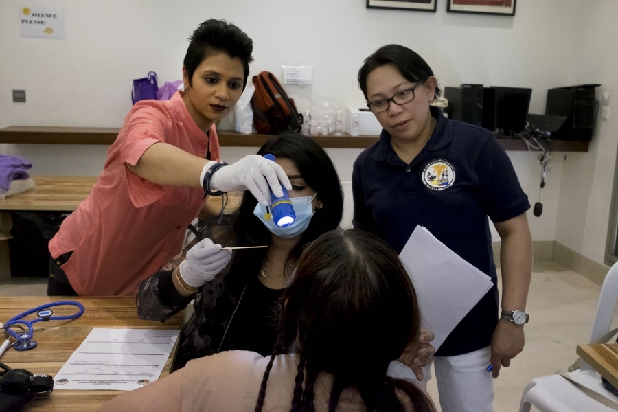 A group of doctors evaluates a patient during a medical mission at the shelter. Around 100 Kuwaitis and Filipino volunteers agreed to help treat over 1,000 domestic workers taking refuge there in March. Credit: Alisa Reznick/PRI 