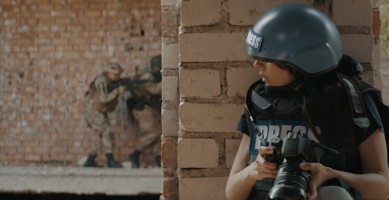 Caucasian female war journalist wearing protective helmet and bulletproof vest gear taking photos during military operation
