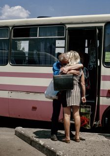 Image of a man and woman hugging in front of a bus. Image description: A bus departing from Kurakhovo, a frontline town, to the entry checkpoint into the non-government controlled Donetsk. After reaching the checkpoint, passengers will have to queue for many hours, in the middle of a mine field, waiting to cross. Despite harsh conditions, over a million people cross this line every month. One of the major reasons for traveling is to visit family members on the other side. Photo by Anastasia Taylor-Lind. Caption by Alisa Sopova..