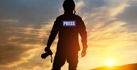 Photojournalist silhouette documenting war or conflict. Photojournalist at sunset. War, army, technology and journalist work concept. Photo credit: Hamara/Shutterstock